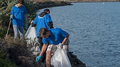 Three people picking up trash by a body of water