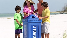 Two parents and two kids at a blue recycle bin at a beach